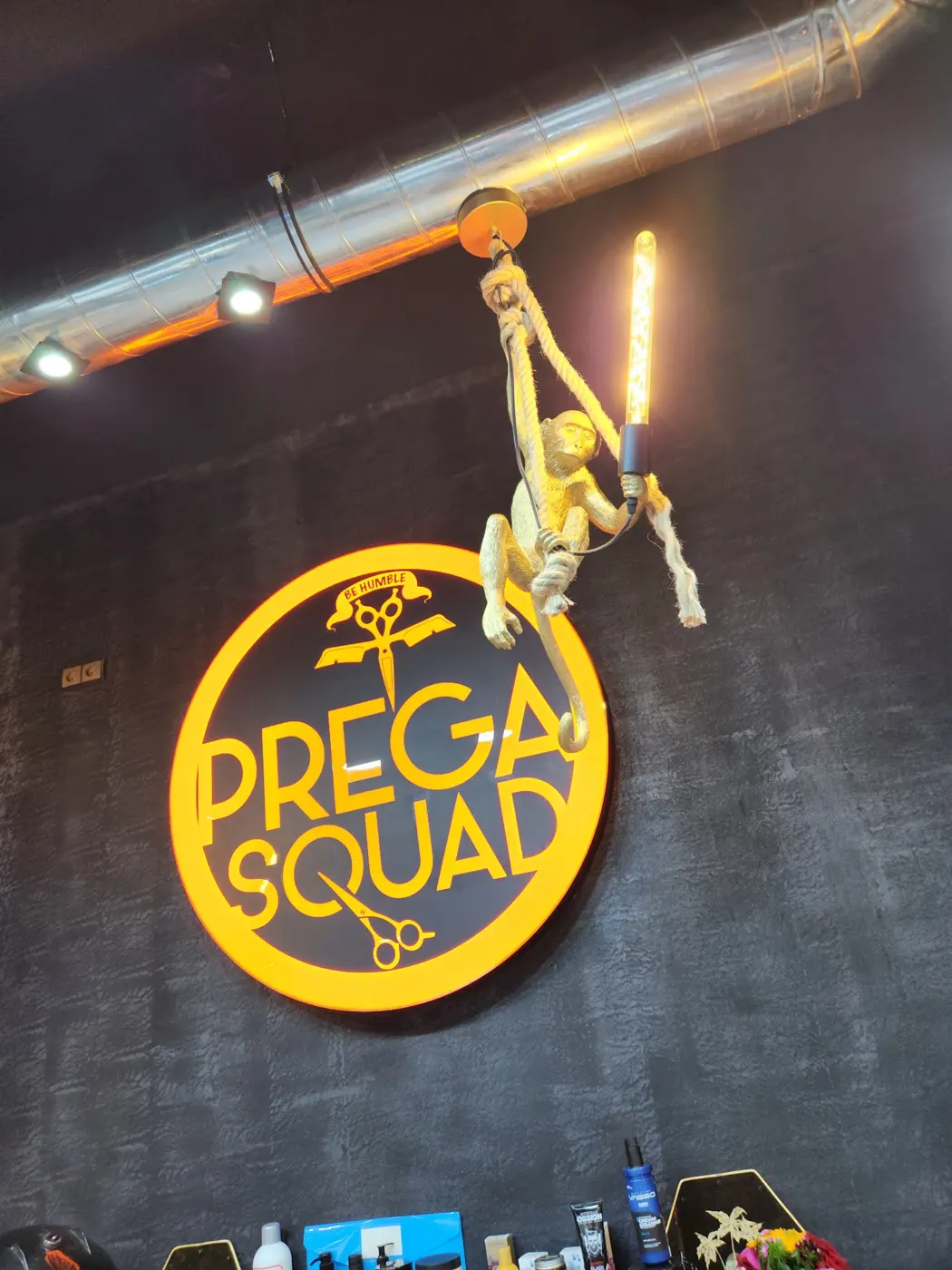 Logo PREGA SQUAD lumineux et lampe singe dorée au mur du salon