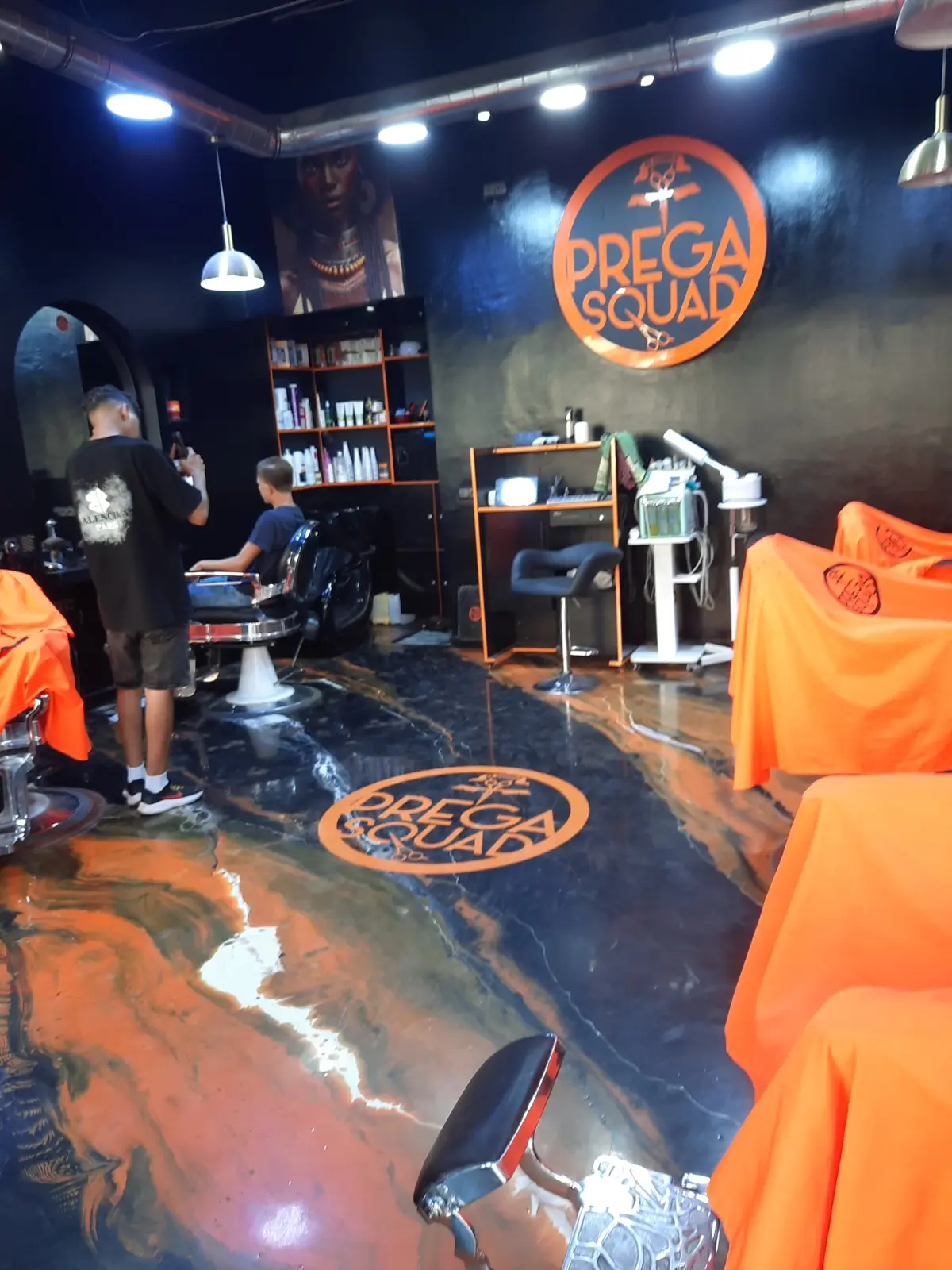 Intérieur du barber shop PREGA SQUAD à Agadir : sol marbré orange, capes orange et logo rouge