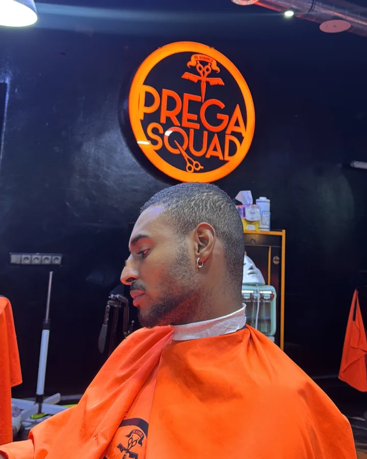 Client avant : cheveux courts bruns, cape PREGA SQUAD, sous le logo du salon